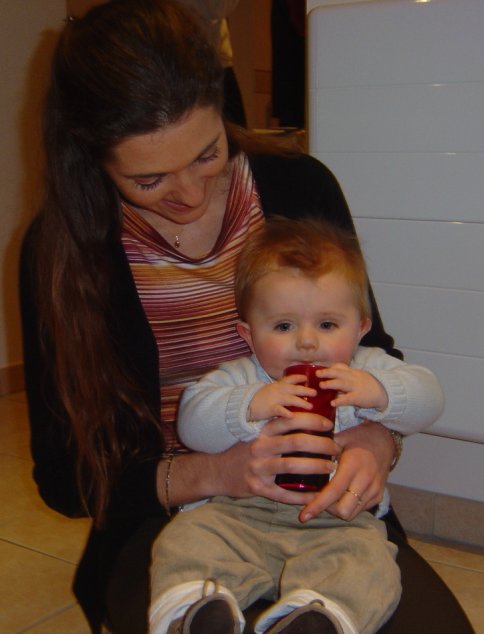 Alexis on Coralie's lap, holding a glass (of coke) and looking content