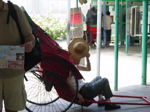 Man resting on his rickshaw and hiding his face with his hat