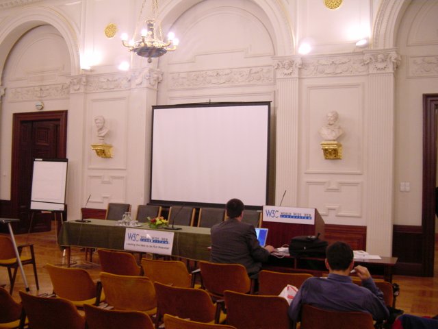 The front of the room: screen, table of speaker, W3C posters, podium