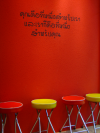 Thai writings on a red wall and red and yellow stools on the floor