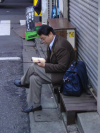 Man sitting in front of a closed shop and reading a book
