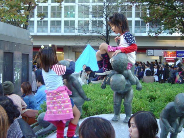 Two little girls climbing bronze statues of kids in front of Shibuya train station