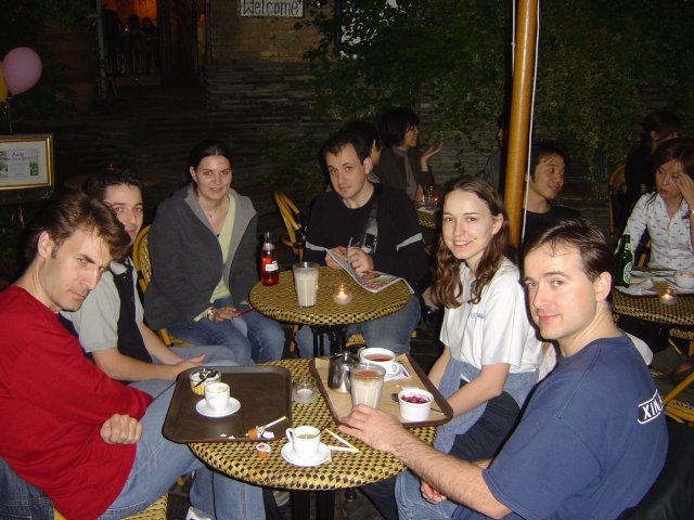 At a cafe: Karl frowning, Vivien, Alex, Hugo, Carine and Yves