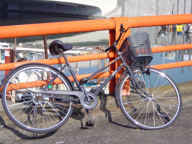 Black bycicle leaning on orange railing on a bridge