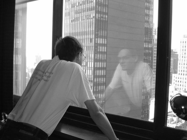 Maxf in front of a large window and his reflection, contemplating the city below