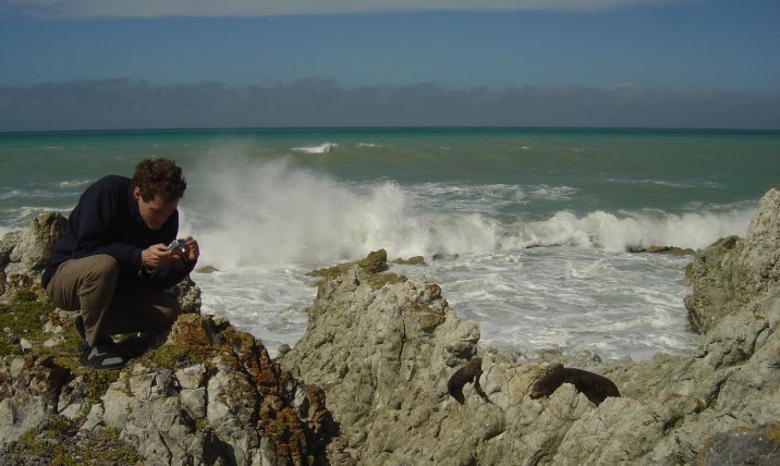 Joel photographying the sea lion, fur seals on the rocks behind, waves of the Pacific ocean