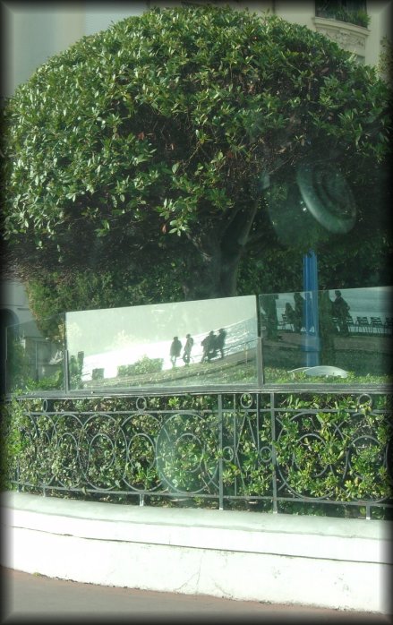 Reflection of the Promenade des Anglais, pedestrians and the sea in the glass fence above the edge of restaurant Chantecler