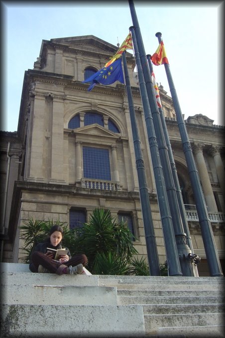 A young woman reading on stairs in front of the MNAC, flags (europe, catalunya, spain, unidentified)