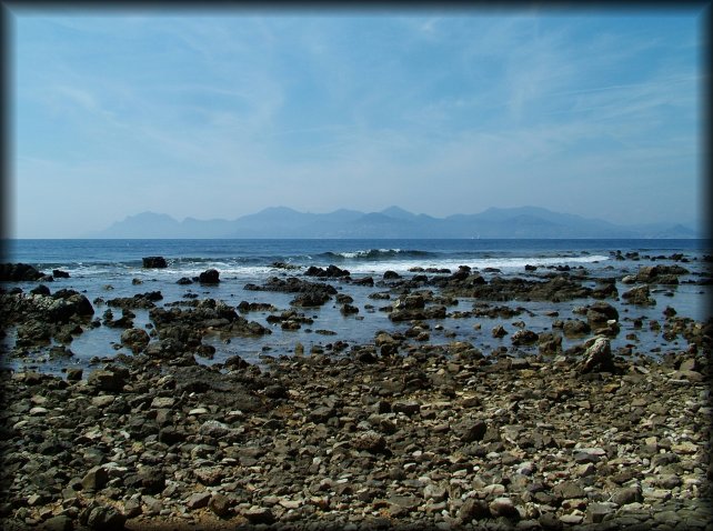 Dark rocks scattered in the water, a wave, the sea and l'Esterel in the background