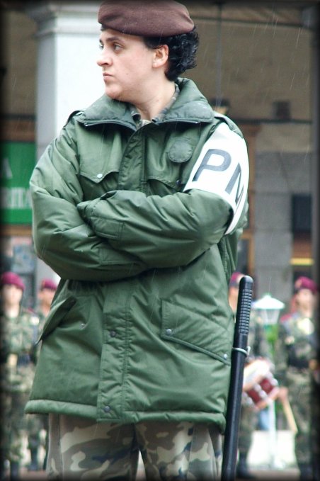 A femal soldier standing under the rain, more soldiers in the background.