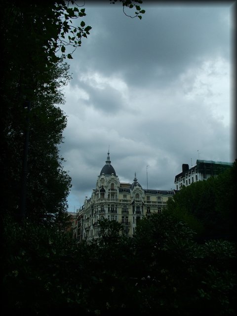 A grey sky over Madrid. An old building rising behind trees.