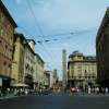 Via Rizzoli in the city centre with torre degli Asinelli and torre Garisenda in the background. City life in the middle-ground, a woman in a red dress crossing the street, a vespa on the left, people.