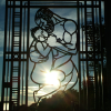 The sun setting slowly behind an iron gate featuring a man protectively cradling an infant. Vigeland Sculpture Park.