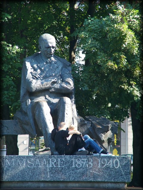 A huge statue of a stern man, looking down on kids seated at his feet.