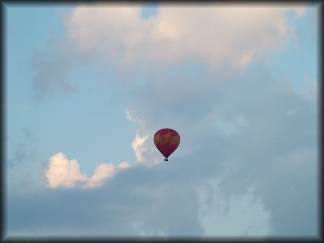 A red balloon in the blue sky against white clouds