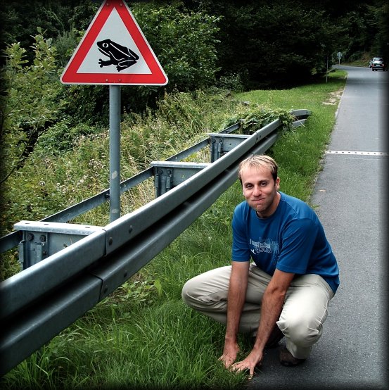 Nicolas pausing as a frog, next to the beware of the frog sign, Eltville am Rhein, Germany