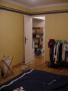 Vue depuis le fond de la chambre: lit, panier a linge, chat, porte donnant sur un hall, portant a coco