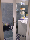 Vue depuis le hall sur la salle de bain: baignoire au fond, dans la miroir de la porte de la salle de bain: lavabo et miroir