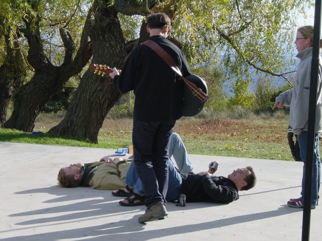 Ted and Gerald lying on the ground, Jose playing the guitar above them, Nicole standing on the right