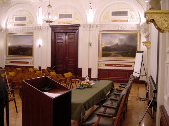 Room of the event: podium, speaker table, screen, rows of chairs, paintings on the wall, etc.