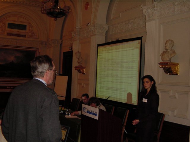 A man from behing, Eva at the podium, Daniel and Marie at the speakers table