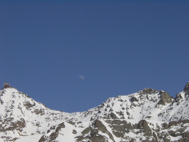 La lune juste au dessus de la montagne enneigee et dans un ciel bien bleu