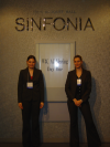 Alex and Coralie standing next to the W3C AC Meeting Day One poster and wearing a similar suit