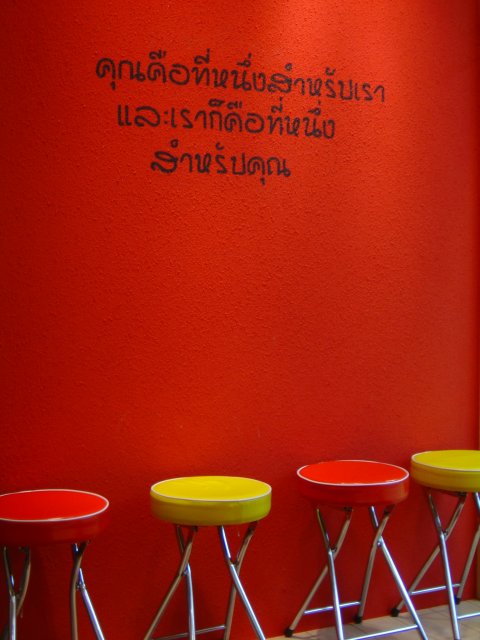 Thai writings on a red wall and red and yellow stools on the floor