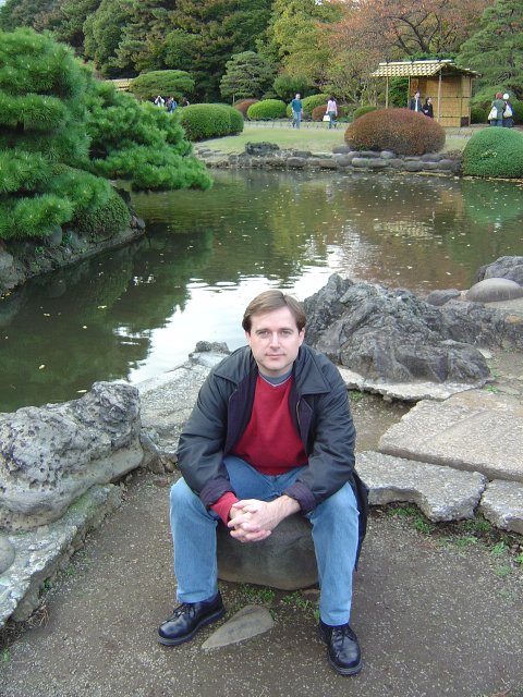 Yves sitting on a stone by a pond