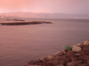 Rose light filtering through the clouds at sunset over a rose sea, fisher under green umbrella