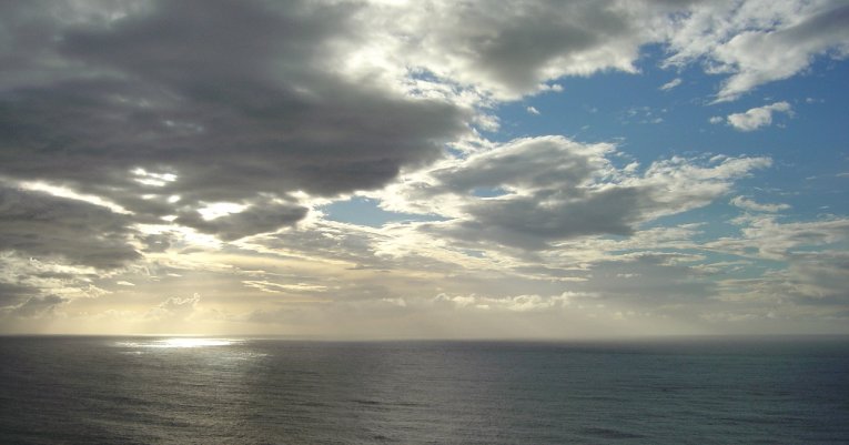Tasman Sea, dark grey water, dark clouds, blue sky behind and a surrealistic patch of light on the water