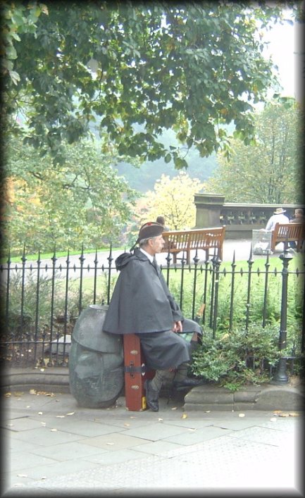 Bagpiper sitting on his bagpipe case by Princes Street Gardens