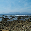 Dark rocks scattered in the water, a wave, the sea and l'Esterel in the background