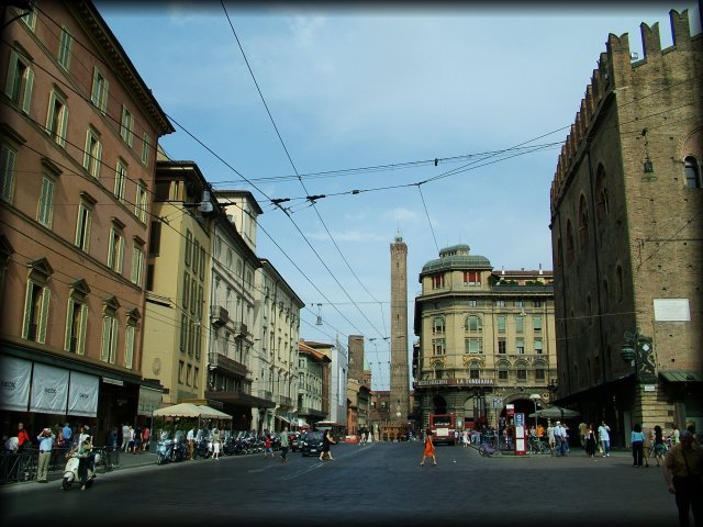 Via Rizzoli in the city centre with torre degli Asinelli and torre Garisenda in the background. City life in the middle-ground, a woman in a red dress crossing the street, a vespa on the left, people.
