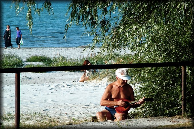 This man was absorbed in his music, his back to the sea, away from the people and near the dirt path. He was playing a mandolin, a happy smile on his face.