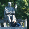 A huge statue of a stern man, looking down on kids seated at his feet.