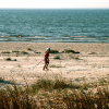 A little girl playing on her own on the beach, dragging a stick in the sand.