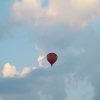 A red balloon in the blue sky against white clouds